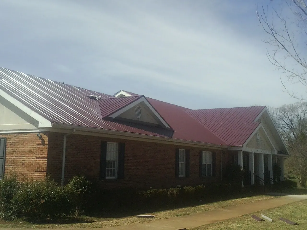 Red metal roof with gabled entries on a long brick building, from a Hail Damage Roof Repair job in Royse City