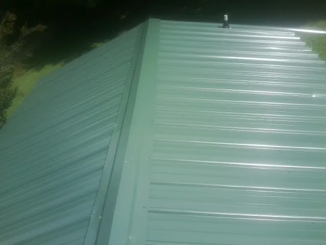 New green metal panels meeting at the ridge of a roof — Flat Roof Repair work by our crew in Royse City