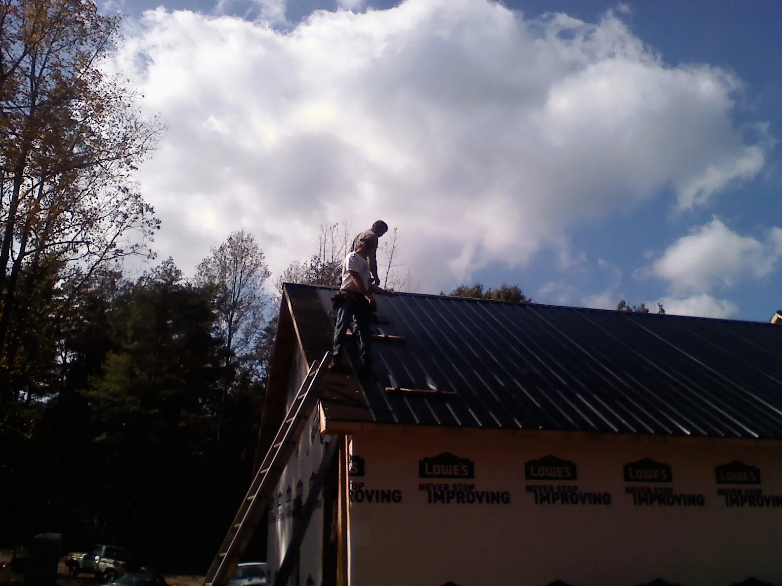 Roofer fastening dark metal panels high against a cloudy sky, from a Roof Inspection job in Royse City