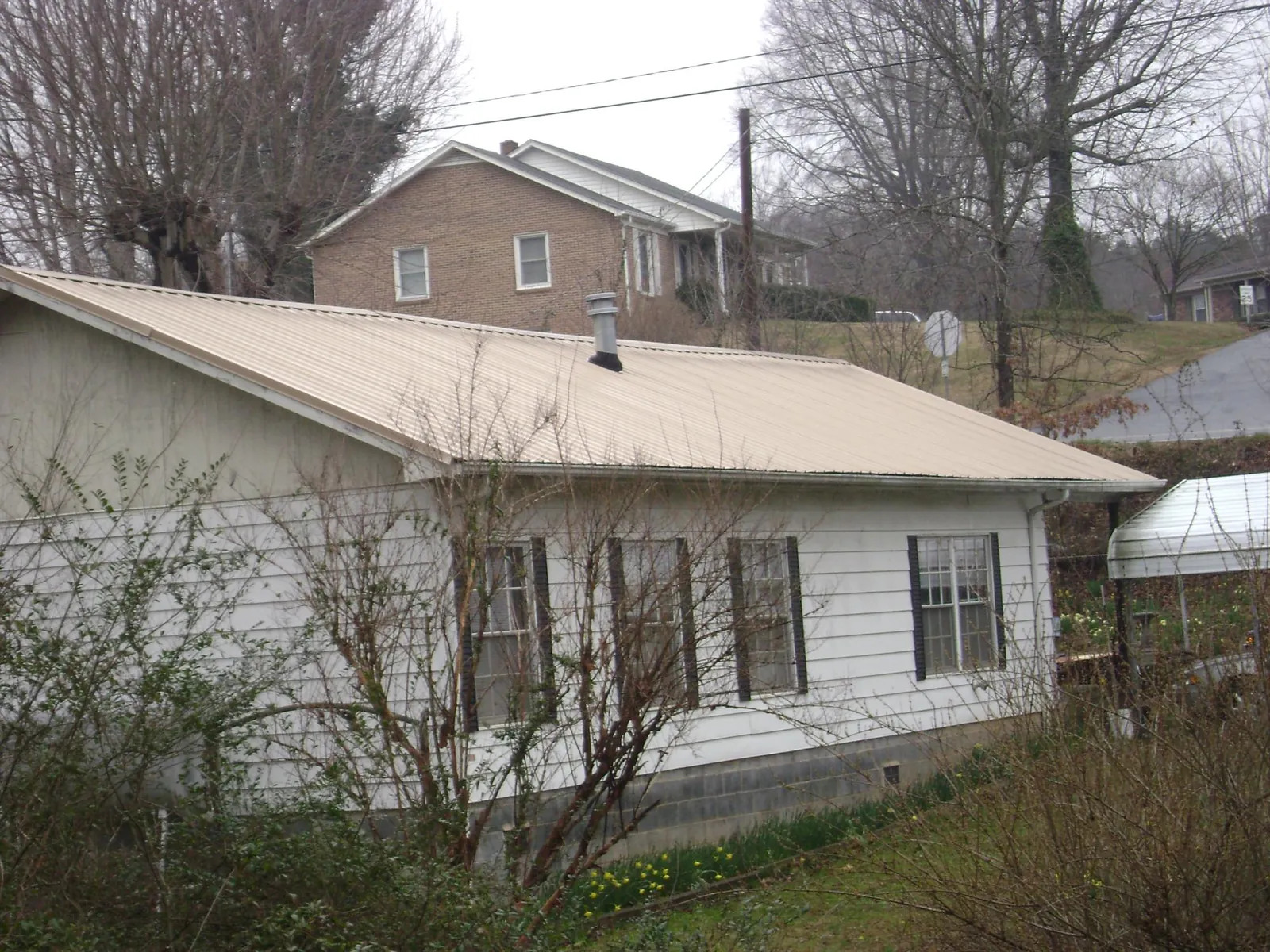 Tan metal roof on a white sided house set into a hillside — Commercial Roofing by Roofing Brothers in Royse City